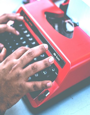 A person's hands typing on a red typewriter